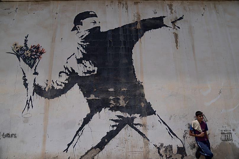 A Palestinian labor rests under a mural by Banksy at a gas station in the West Bank city of Bethlehem - 2022