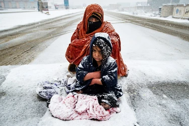 Афғонистонлик аёл ва унинг боласи совуқ кунда Кобулдан чиқаётган йўлда ўтаётган машиналардан пул сўрамоқда